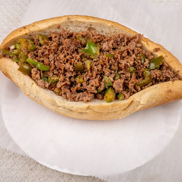 A Pete's-A-Place cheesesteak sandwich, filled with chopped meat and green peppers, on a white plate.