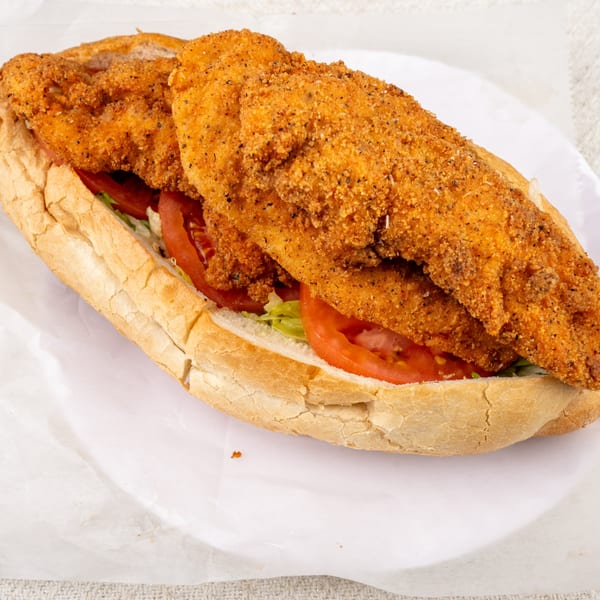 Crispy fried chicken sandwich with lettuce and tomatoes on a white plate.