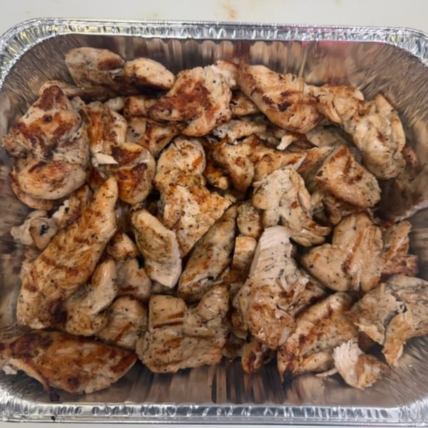 Grilled chicken pieces, seasoned and browned, in a foil catering pan from Pete's-A-Place.