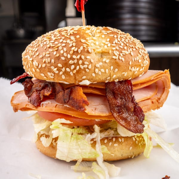 A large sandwich with turkey, bacon, lettuce, and tomato on a sesame seed bun.