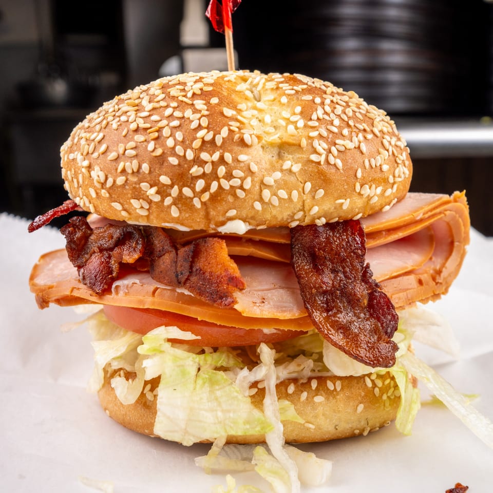 A large sandwich with turkey, bacon, lettuce, and tomato on a sesame seed bun.