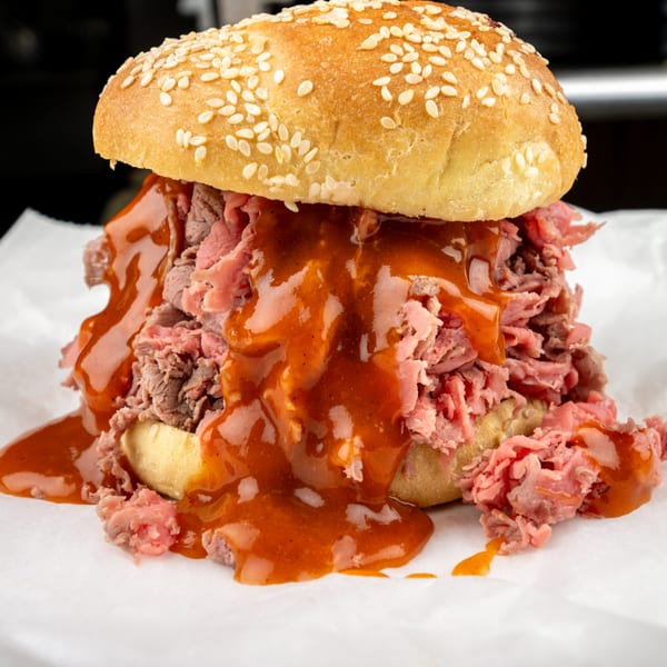 A roast beef sandwich with barbecue sauce on a sesame seed bun, on white paper.