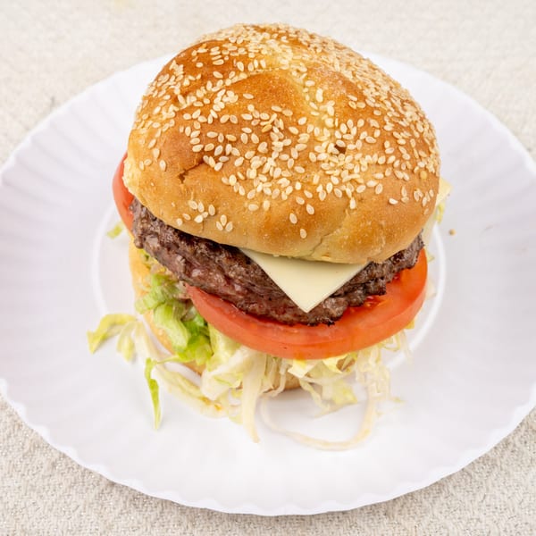 A Pete's-A-Place cheeseburger with lettuce and tomato on a sesame seed bun, served on a white plate.