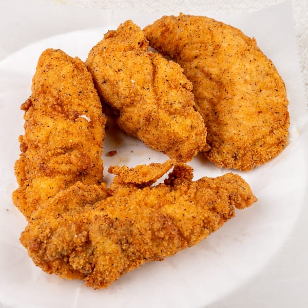 Crispy, golden-brown chicken tenders seasoned with black pepper, served on a white plate.