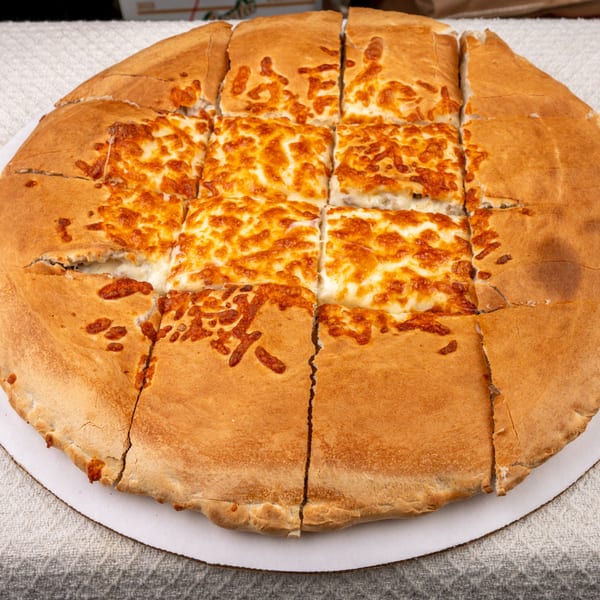 A large, round Pete's-A-Place cheese pizza, cut into squares, with a thick golden crust.
