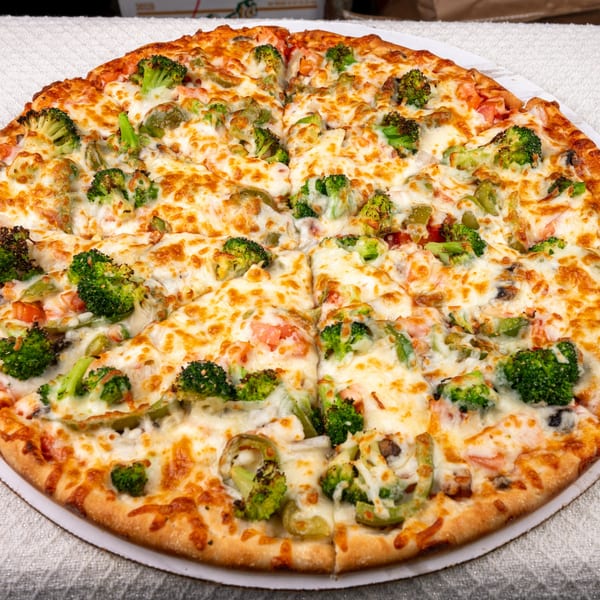Pete's-A-Place pizza with melted cheese, broccoli, green peppers, and tomatoes, sliced into eight pieces.