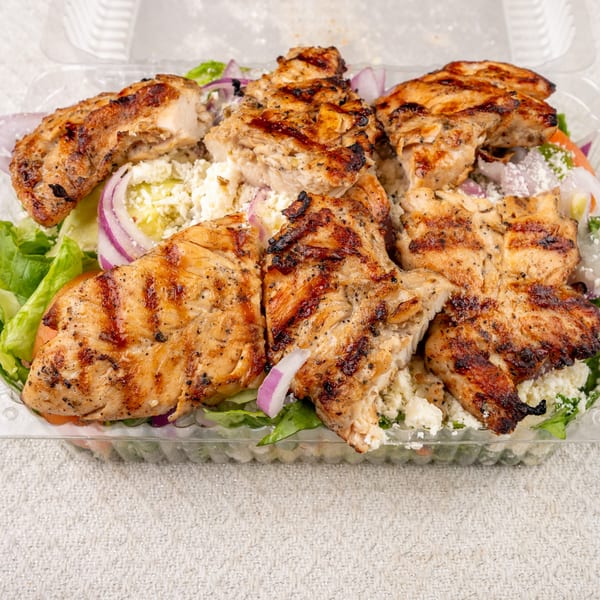 Grilled chicken pieces with char marks on a bed of salad greens, red onion, and feta cheese.